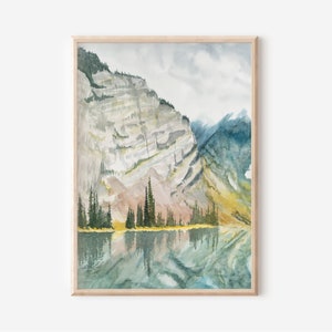 Pode incluir: Pintura em aquarela de uma paisagem de montanha com um lago. A obra apresenta uma moldura de madeira clara, uma montanha com tons cinza e amarelo e um lago que reflete o céu e as montanhas. As árvores perenes margeiam a borda do lago.
