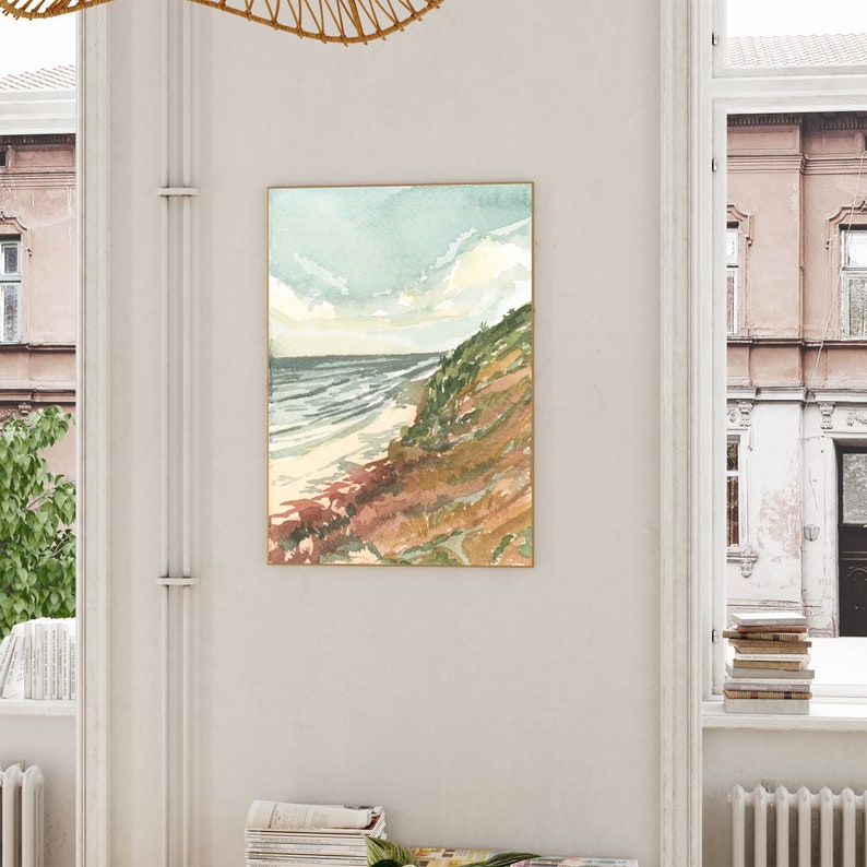 May include: A framed vertical wall art print featuring a watercolor landscape painting of a coastal scene. The artwork depicts a sandy beach meeting the ocean under a pale sky, with a grassy, textured cliffside in shades of green and brown.