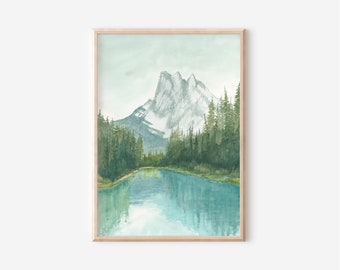 May include: A watercolor painting in a light wood frame depicting a snow-capped mountain peak rising above a dense forest of dark green pine trees, with a calm, reflective blue lake in the foreground under a pale, soft sky.