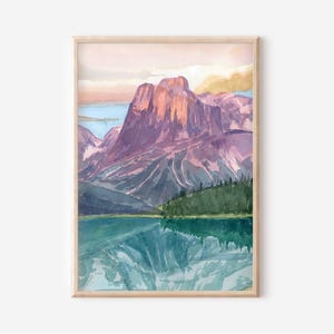 Könnte beinhalten: Aquarellmalerei einer Berglandschaft mit einem See. Das Kunstwerk zeigt eine große violette Bergkette, einen türkisfarbenen See und einen grünen Wald. Der Himmel hat rosa und gelbe Farbtöne, und das Kunstwerk ist in einem hellen Holzrahmen gerahmt.