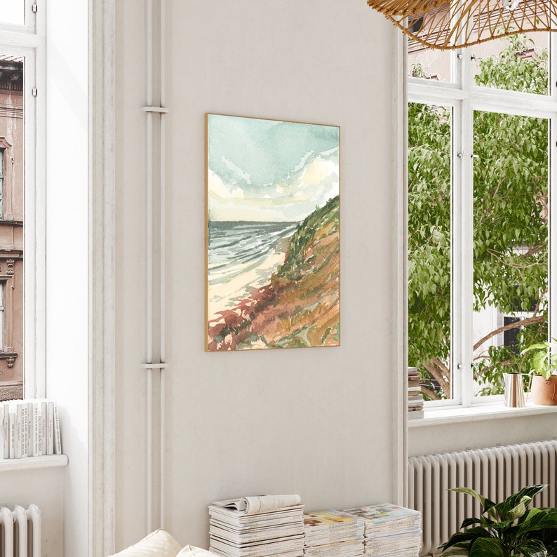 May include: A vertical rectangular wall art print featuring a watercolor landscape of a coastal cliffside meeting the ocean. The scene displays a sandy beach, rolling waves, and a grassy hillside in shades of green, brown, and soft blue sky.