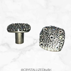 May include: Two square-shaped crystal drawer pulls with a silver base. The pulls are covered in clear rhinestones.
