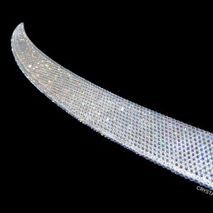May include: A curved, shimmering band densely covered in small, clear crystals. The crystals catch the light, creating a sparkling effect against the black background. The text "CRYSTALLIZEDbyBri.com" is visible at the bottom right.