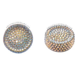 May include: Two round, flat, silver-toned, crystal-covered, decorative objects. The crystals are iridescent and have a rainbow effect. The text "CRYSTALLIZEDbyBri.com" is printed on the top of each object.