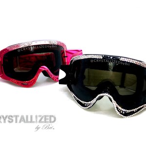 K&ouml;nnte beinhalten: Zwei Paar verzierte Skibrillen. Ein Paar ist rosa mit einem Wirbelmuster und roten Kristallakzenten. Das andere Paar ist schwarz mit silbernen Kristallakzenten. Der Text "CRYSTALLIZED by Bri" steht unten.