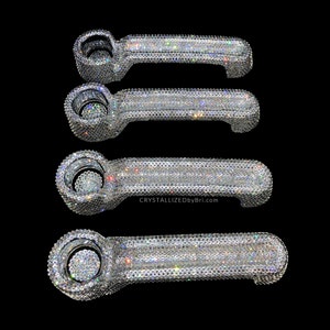 May include: Four crystal-covered pipes, each with a bowl and a stem, are displayed against a black background. The pipes are encrusted with sparkling crystals, reflecting light. The website address "CRYSTALLIZEDBYBri.com" is visible.