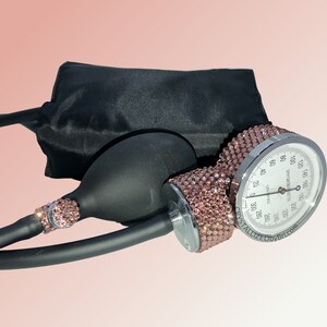 May include: A black blood pressure cuff with a silver gauge and a pink rhinestone-covered pump. The gauge reads "CRYSTALLIZED BY BTI.COM".
