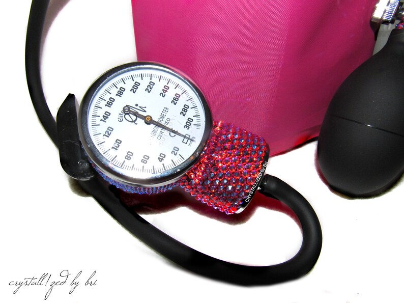 May include: A red and black blood pressure monitor with a crystal-encrusted cuff. The gauge reads up to 300 mmHg and is labeled "Sphygmomanometer Certified".