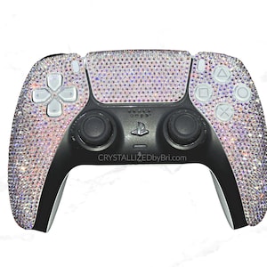 May include: A black and silver video game controller bedazzled with iridescent crystals. The controller features white buttons and the text "CRYSTALLIZEDbyBri.com". The controller is designed for a gaming console.