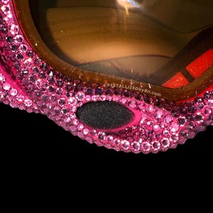 K&ouml;nnte beinhalten: Nahaufnahme einer pinkfarbenen Skibrille, die stark mit kleinen, glitzernden Kristallen verziert ist. Die Brille hat einen braunen Rahmen und ein schwarzes Nasenst&uuml;ck aus Schaumstoff. Der Text "CRYSTALLIZEDbyBri.com" ist sichtbar.
