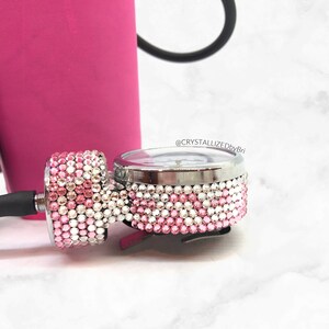 May include: A close-up of a silver medical blood pressure gauge with a pink and white rhinestone design. The gauge is attached to a black blood pressure cuff.