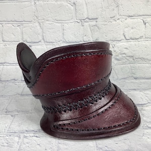 Könnte beinhalten: Ein burgunderfarbener Lederkragen mit schwarzen Nähten und einer dekorativen Klappe. Der Kragen hat ein einzigartiges Design mit mehreren Schichten und einer spitzen Form.