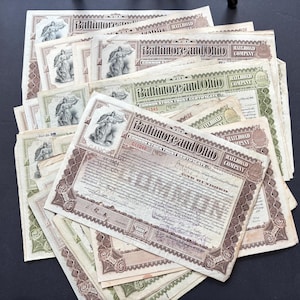 May include: A collection of vintage Baltimore and Ohio Railroad Company stock certificates. The certificates feature ornate borders, detailed text, and an illustration of a classical figure. The certificates are in various shades of green, brown, and beige.
