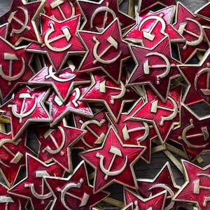 Puede incluir: Primer plano de una colección de insignias rojas en forma de estrella con emblemas dorados de martillo y hoz. Las insignias tienen una superficie texturizada y un borde dorado. Las insignias están dispuestas juntas, llenando el marco.