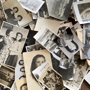 May include: A pile of black and white photographs, some with people in them, others with landscapes or buildings. The photos are arranged in a random order, and some are overlapping.