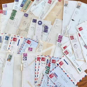 May include: A selection of vintage envelopes, many with colourful postage stamps and postmarks. The envelopes vary in size and shade of white and cream, some with red, white, and blue airmail borders. The stamps display different colours and designs.