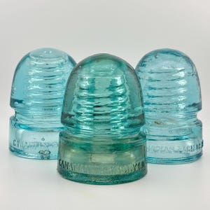 May include: Three vintage light blue glass electrical insulators with a rounded dome top and ribbed sides. Each piece features the embossed text CANADIAN PACIFIC RY CO along the base, showcasing a translucent finish and a sturdy, cylindrical shape.