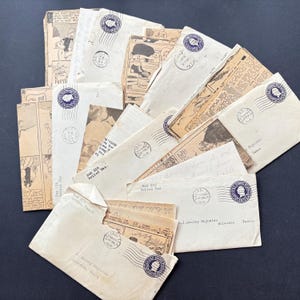 May include: A selection of antique envelopes and ephemera, displaying stamps, handwritten addresses, and printed text. The envelopes are cream-coloured with blue stamps and various markings. Some envelopes contain comic strips and newspaper clippings.
