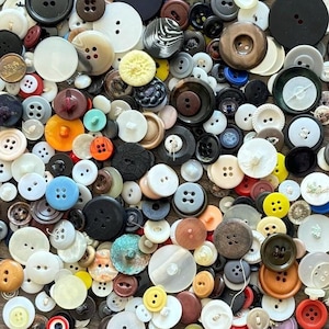 May include: A large collection of assorted buttons in various shapes, sizes, and colours including white, black, brown, blue, orange, yellow, and red. The buttons feature different designs, including two-hole and four-hole styles, with smooth, textured, and patterned surfaces.