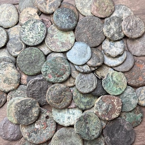 Peut inclure: Une collection de pièces de monnaie antiques de tailles et de formes variées. Les pièces présentent une gamme de couleurs, notamment des nuances de vert, de brun et de gris, avec des signes visibles d'usure et d'âge. Les pièces sont éparpillées, créant une surface texturée.