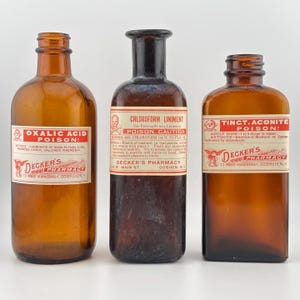 May include: Three antique brown glass apothecary bottles with labels. The labels read "Oxalic Acid Poison!", "Chloroform Liniment Poison Caution", and "Tinct. Aconite Poison!". Each bottle has a label from Decker's Pharmacy.