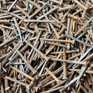 May include: A close-up shot of a pile of rusty, square-headed nails. The nails are various sizes and are scattered in a haphazard manner. The metal has a weathered, aged appearance, with shades of brown and gray.