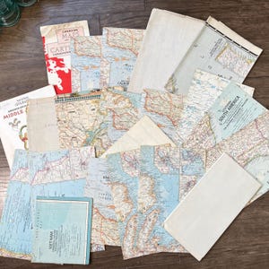 May include: A collection of vintage National Geographic paper maps and map covers featuring various regions including South America, Canada, and Southeast Asia. The assortment includes folded cartographic documents with printed text, geographic details, and white paper sleeves.