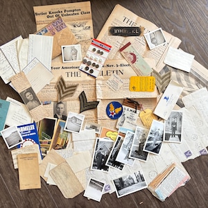 Op de afbeelding: Een verzameling vintage memorabilia, waaronder krantenknipsels, foto's, brieven en militaire insignes. De items zijn gerangschikt op een houten oppervlak en tonen een verscheidenheid aan historische documenten en memorabilia.