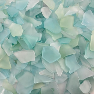 Puede incluir: Primer plano de trozos de vidrio de mar en varios tonos de azul, verde y blanco. Las piezas tienen forma irregular y un aspecto liso y esmerilado. El vidrio de mar está disperso, creando una superficie texturizada.