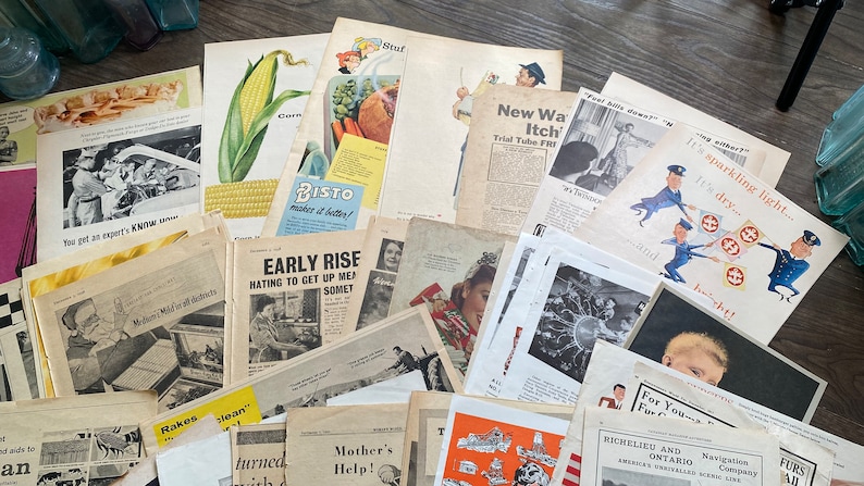 May include: A collection of vintage ephemera, including advertisements, newspaper clippings, and magazine pages. The items feature illustrations of food, people, and products, with text in English. The papers are arranged on a wooden surface.