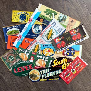 Peut inclure: Une collection d'étiquettes alimentaires vintage, avec des marques comme "Blue Cross Tea", "Genie Tuna" et "King's Tomatoes". Les étiquettes présentent des graphiques colorés de légumes, de fruits et d'autres aliments, avec du texte varié.