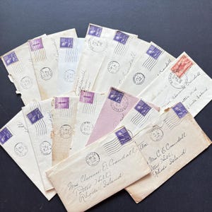 May include: A collection of vintage white and off-white paper envelopes arranged in a fan shape. Each envelope features a purple or red postage stamp, black ink postmarks, and handwritten addresses in cursive script addressed to Mrs. C. E. Crandall.