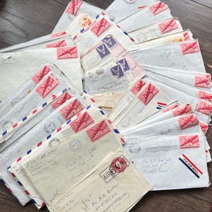 May include: A pile of vintage airmail envelopes, with red and blue striped borders, stamps, and handwritten addresses. The envelopes show various postmarks and a "VIA AIR MAIL" sticker.