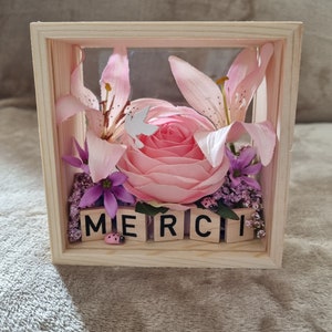 Caja con marco de madera en bruto decorada en su interior con la letra de flor morada de lirio ranúnculo "GRACIAS"