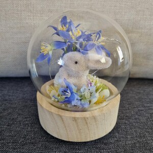 Bola de Pascua de cristal decorada a mano con un conejo, una estrella austral, una flor de viburno, huevos de Pascua y una luz con la inscripción "BURBUJA DE PASCUA".