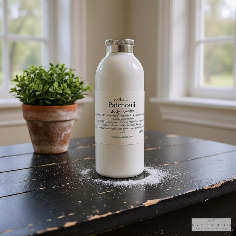 May include: A white body powder bottle with a silver cap and the text "Patchouli Body Powder." A small potted plant sits to the left. The bottle is on a black wooden surface with powder sprinkled around it.