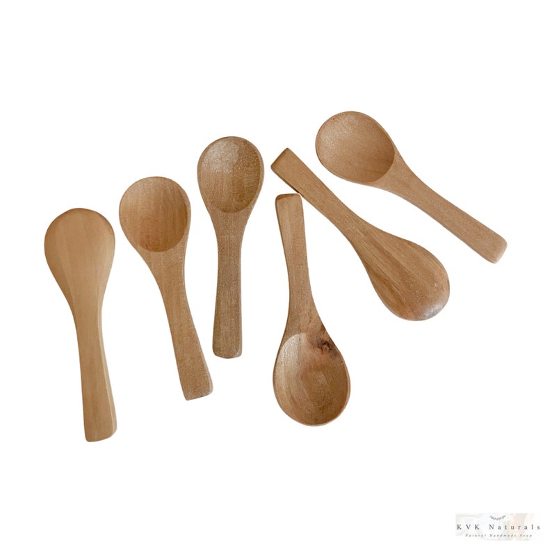 May include: Six small, light brown wooden spoons are arranged on a white background. Each spoon has a rounded bowl and a slender handle. The spoons vary slightly in shape and size, showcasing natural wood grain.