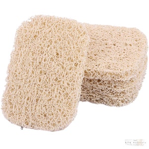 May include: A stack of beige, rectangular loofah sponges. The sponges have a woven, open texture. One sponge is separated from the stack, showing its shape. The loofahs are a natural color and appear to be made from plant fibers. The image is well-lit.