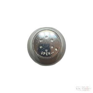 May include: A silver metal shaker top with a circular design. The top has several small holes and the word "OPEN" is printed on the surface. The shaker top is designed to dispense contents.
