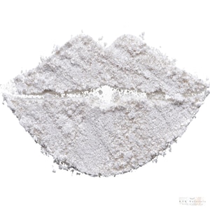May include: A close-up of a white powder arranged in the shape of lips. The powder has a granular texture and is set against a white background. The bottom right corner of the image has the text "KVK Naturals".