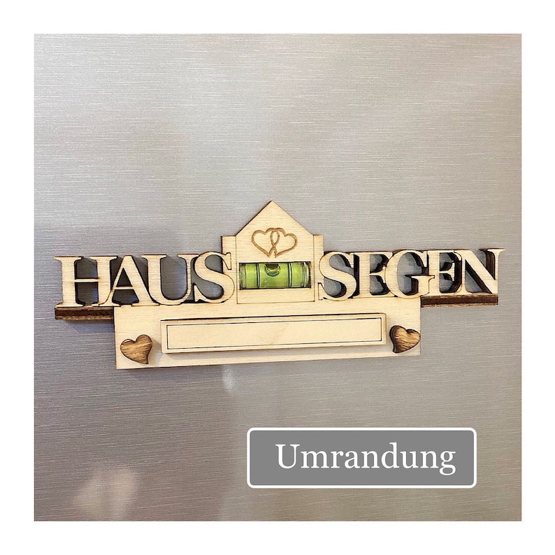 May include: A wooden sign with the German words "HAUS SEGEN" and a small level. The sign has a house-shaped top with two hearts and a rectangular space for personalization. Two wooden hearts flank the rectangular space.
