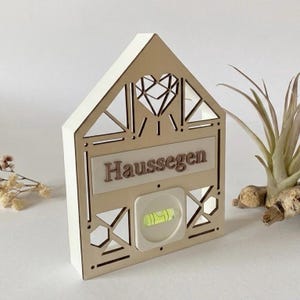 Könnte beinhalten: Holzhaus-Dekoration mit dem Wort "Haussegen" und einer Wasserwaage. Das Haus hat ein geometrisches Design mit einem herzförmigen Ausschnitt. Die Wasserwaage befindet sich in einem Quadrat, und das Holz hat eine natürliche Oberfläche.