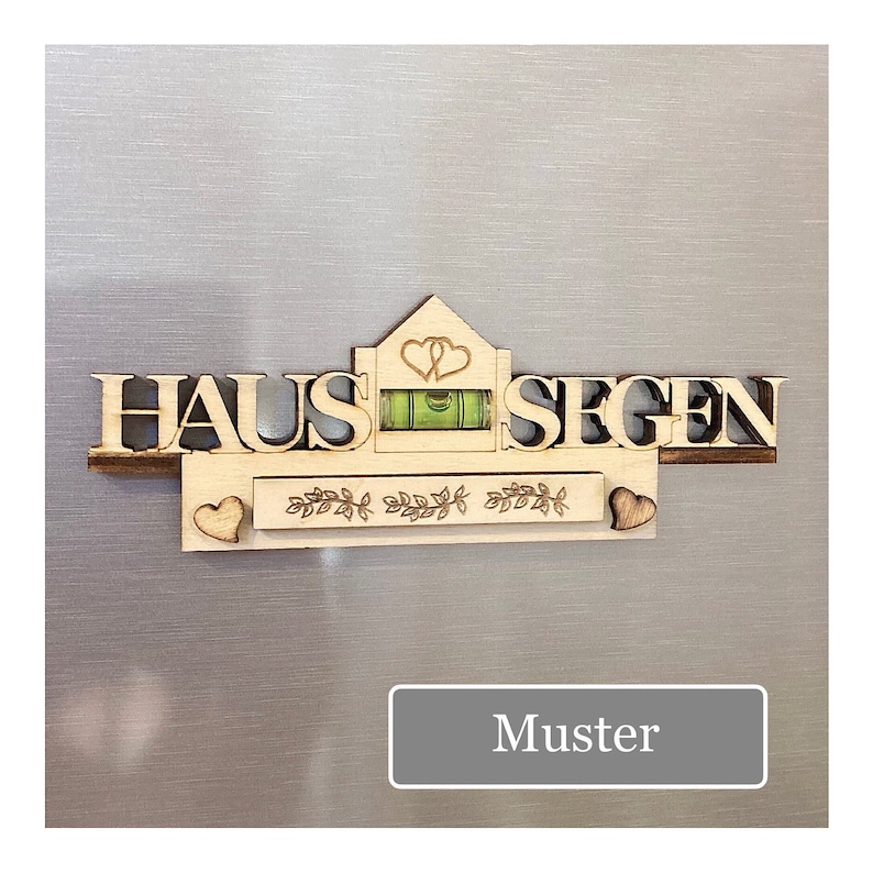 May include: Wooden wall decor with the German words "HAUS SEGEN" and a level. The design includes a house shape with two hearts, a decorative border, and two small hearts. The word "Muster" is in a gray rectangle.