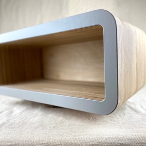 May include: A light gray floating shelf with rounded edges and a wood grain finish. The shelf is empty and ready to display items.
