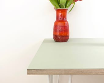 May include: A light green table with white hairpin legs and a red and orange ceramic vase with a bouquet of yellow and red tulips.
