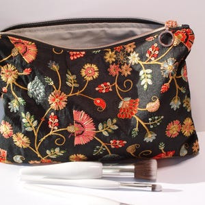 May include: Black velvet makeup bag with a floral embroidery design featuring red, orange, and green flowers. The bag has a zipper closure and a silver ring pull.