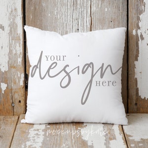 Puede incluir: Almohada blanca con el texto "Your design here" sobre un fondo de madera r&uacute;stico.