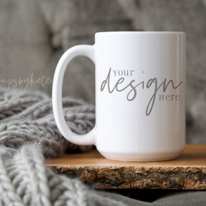 Puede incluir: Taza de café de cerámica blanca con asa, sobre una superficie de madera. La taza tiene el texto "YOUR DESIGN HERE" impreso en la parte delantera.