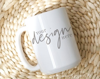May include: White ceramic mug with a handle, sitting on a woven straw mat. The mug has the text "Your design here" printed on it in a gray cursive font.