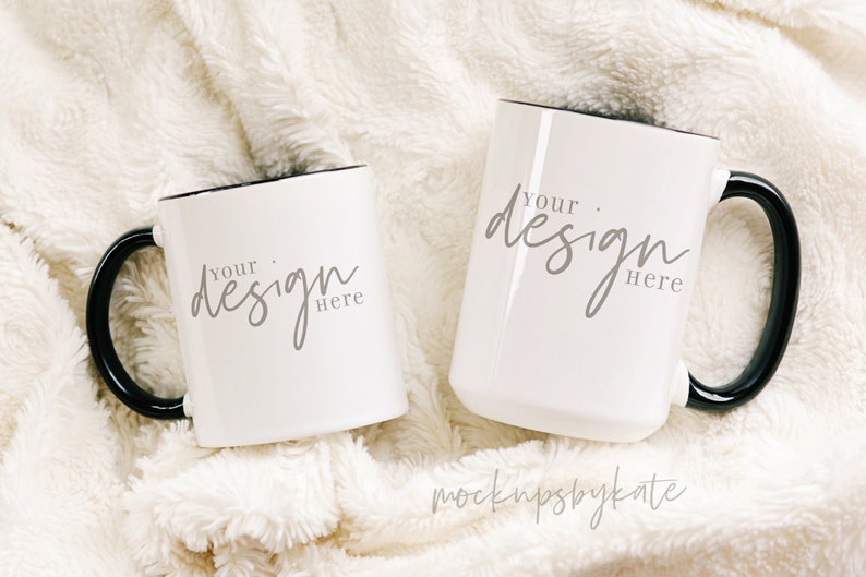 Może przedstawiać: Dwa białe ceramiczne kubki z czarnymi uchwytami i czarnymi obw&oacute;dkami. Kubki leżą na białym, puszystym kocu. Tekst "Your design here" jest napisany szarym kolorem na każdym kubku.